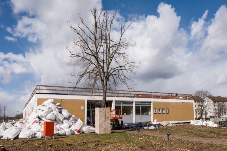 Bauarbeiten an einem eingeschossigen Gebäude mit Materialhaufen und Baugerüst