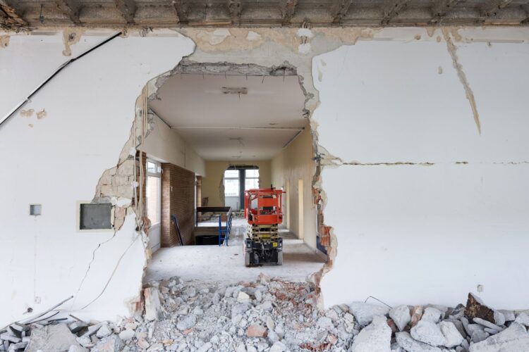 Blick durch eine Wandöffnung auf eine Baustelle im Innenraum mit Bauschutt und Arbeitsgerät