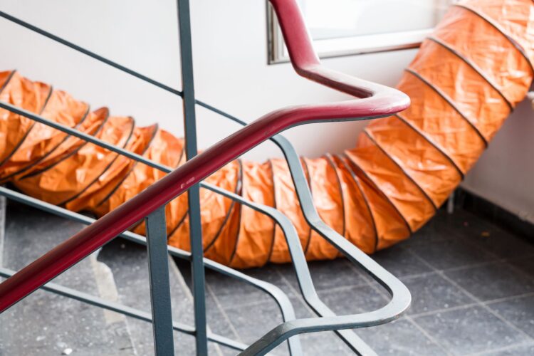 Treppenhaus mit orangefarbenem Lüftungsschlauch und Geländer