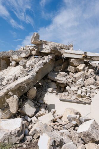 Trümmer und Bauschutt einer abgerissenen Betonmauer vor blauem Himmel
