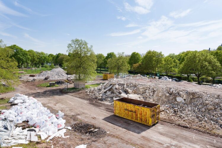 Baufläche mit Bauschutt und gelbem Container im Grünen