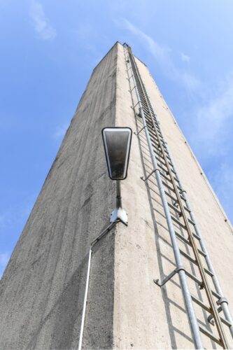 Betonwand mit senkrechter Leiter und Lampe vor blauem Himmel